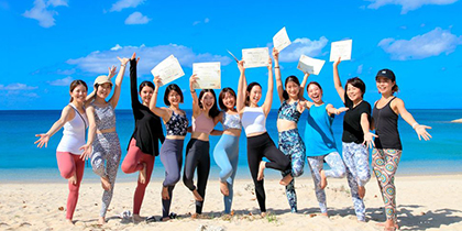 沖縄の海の前で証書を手に喜ぶ卒業生たち